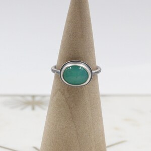Op de afbeelding: Een zilveren ring met een groene ovale edelsteen in een bezel-setting. De ringband is getextureerd.