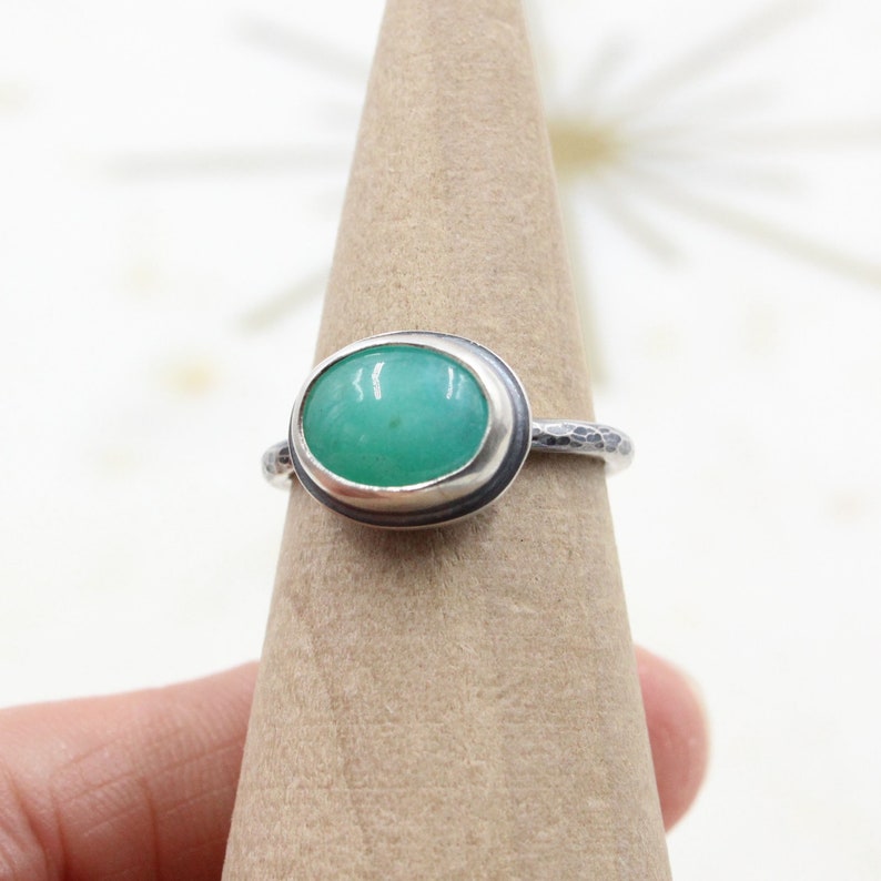 Op de afbeelding: Een zilveren ring met een groene ovale edelsteen in een bezel setting. De band is getextureerd.