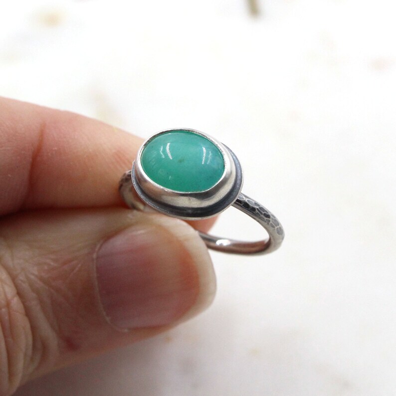 Op de afbeelding: Een zilveren ring met een groene edelsteen in een bezel-setting. De band is getextureerd.