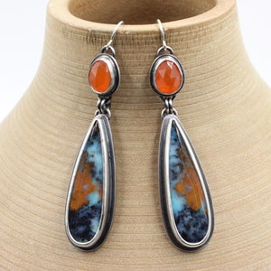 May include: A pair of silver dangle earrings with teardrop-shaped orange and blue agate stones and smaller round orange carnelian stones.