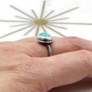 Op de afbeelding: Een zilveren ring met een turquoise edelsteen in een bezel-setting. De band is gehamerd en heeft een textuur.
