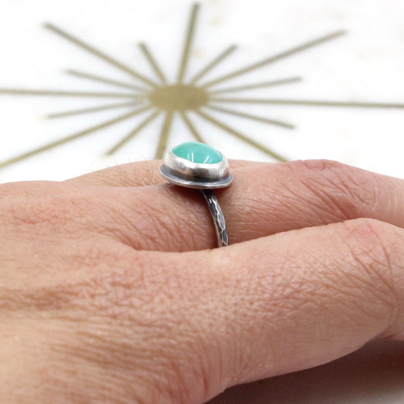 Op de afbeelding: Een zilveren ring met een turquoise edelsteen in een bezel-setting. De band is gehamerd en heeft een textuur.