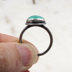 Op de afbeelding: Een zilveren ring met een groene edelsteen gezet in een bezel setting. De ringband is getextureerd en heeft een gehamerde afwerking.