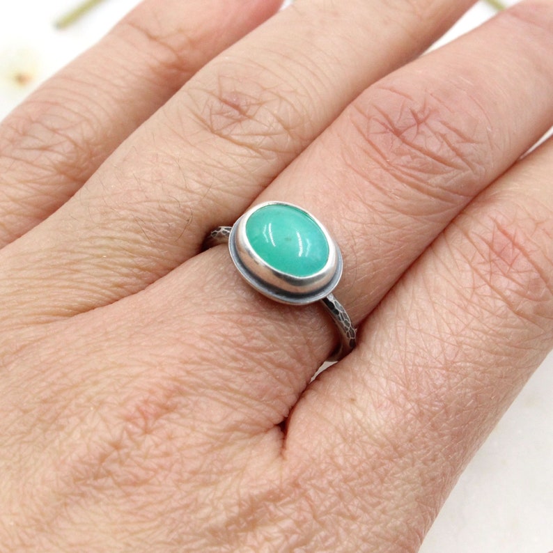 Op de afbeelding: Een zilveren ring met een groene ovale edelsteen in een bezel setting. De band is getextureerd.