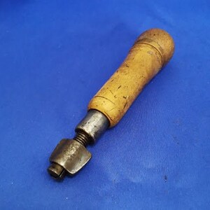 May include: A vintage leather working tool with a wooden handle and a metal head. The tool is used for punching holes in leather.