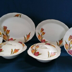 May include: A set of six white ceramic plates with a floral design featuring yellow and orange tulips. The set includes two oval platters, two round dinner plates, and two covered bowls.