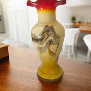 May include: A small, decorative vase with a wavy, marbled design in shades of yellow, white, and grey. The vase has a red and orange rim.