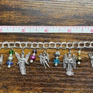May include: A silver charm bracelet with angel charms and colorful beads. The bracelet is approximately 8 inches long. The charms include detailed angel figures and various bead accents in red, green, blue, and pink.