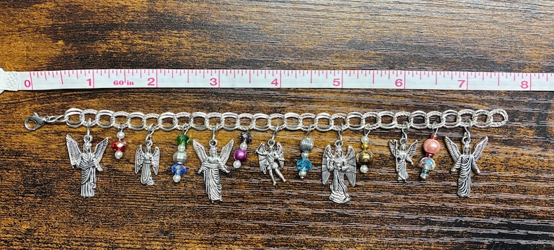 May include: A silver charm bracelet with angel charms and colorful beads. The bracelet is approximately 8 inches long. The charms include detailed angel figures and various bead accents in red, green, blue, and pink.