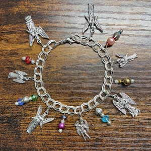 May include: A silver charm bracelet featuring multiple angel charms and colorful beads. The bracelet has a chain link design with a lobster clasp closure. The charms include detailed angel figures and winged designs, with beads in various colors.