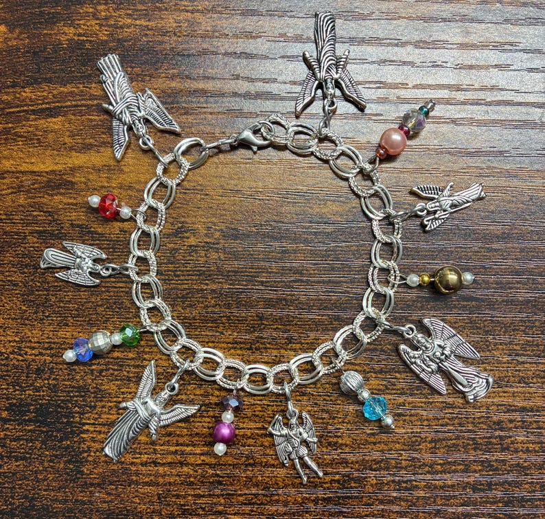 May include: A silver charm bracelet featuring multiple angel charms and colorful beads. The bracelet has a chain link design with a lobster clasp closure. The charms include detailed angel figures and winged designs, with beads in various colors.