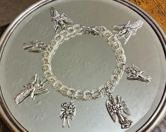 May include: A silver-toned charm bracelet featuring a double-link chain design. The bracelet is adorned with six distinct metal charms, each depicting a winged figure or angel in a metallic silver finish, evenly spaced around the circular chain.
