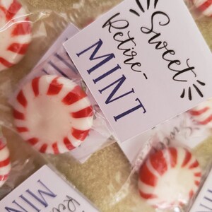 May include: A white card with the text "Sweet Retire-Mint" in black cursive writing. The card is next to a small clear plastic bag containing a red and white peppermint candy.