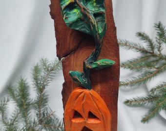 May include: A carved wooden Halloween decoration featuring an orange jack-o'-lantern with a smiling face and a green leaf. The pumpkin is attached to a brown wooden base. The leaf and pumpkin are painted with green and orange hues.