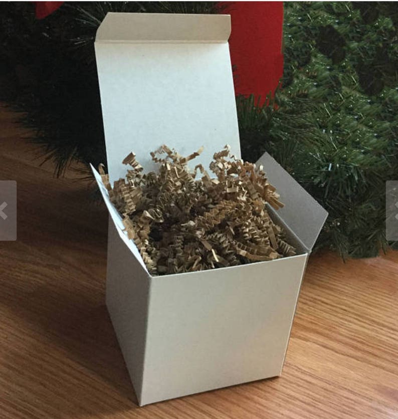 May include: A white cardboard box with a lid open, revealing brown packing paper inside. The box is sitting on a wooden surface.