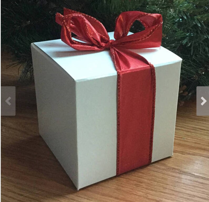 May include: A white gift box with a red satin ribbon tied in a bow. The box is sitting on a wooden surface.