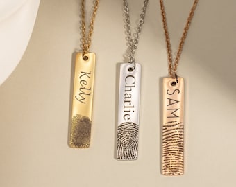 May include: Three gold, silver, and rose gold necklaces with personalized bar pendants. Each pendant features a fingerprint design and a name engraved on the front: Kelly, Charlie, and Sam.