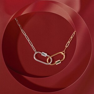 May include: A silver and gold chain necklace with two linked oval-shaped charms. The necklace is photographed on a red background.