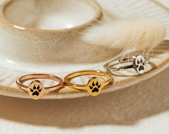 May include: Three silver rings with a paw print design. The rings are on a white plate with a brown rim.