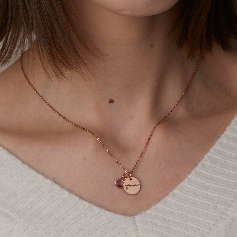 May include: A rose gold necklace with a small round pendant that says "jasmine" in cursive. The pendant is attached to a small rose gold gemstone.