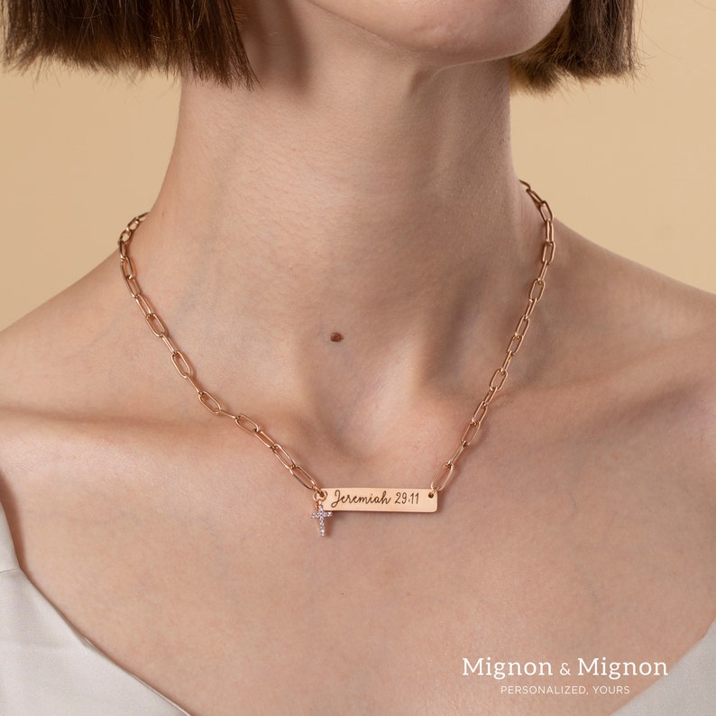 May include: A rose gold chain necklace with a small cross charm and a rectangular pendant engraved with the text "Jeremiah 29:11".