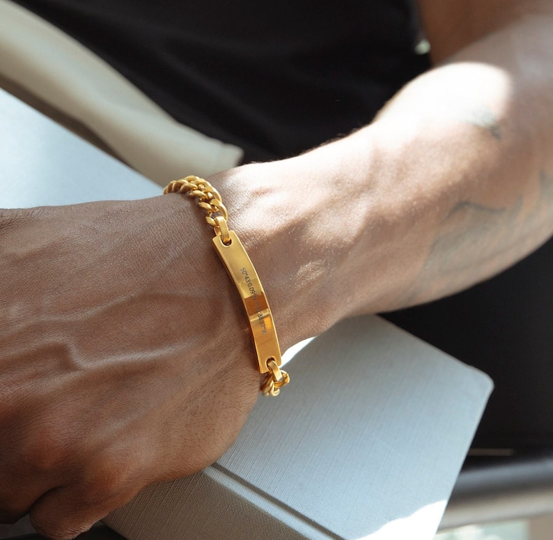Pode incluir: Um bracelete de corrente dourada com uma etiqueta retangular que diz "Gratid&atilde;o &eacute; a melhor atitude".