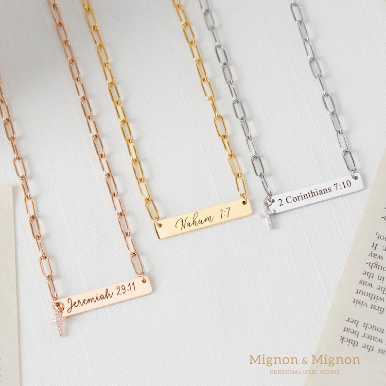 May include: Three gold, silver, and rose gold necklaces with a small cross charm and a rectangular bar pendant with engraved text. The text on the pendants reads "Nahum 1:7", "2 Corinthians 7:10", and "Jeremiah 29:11".
