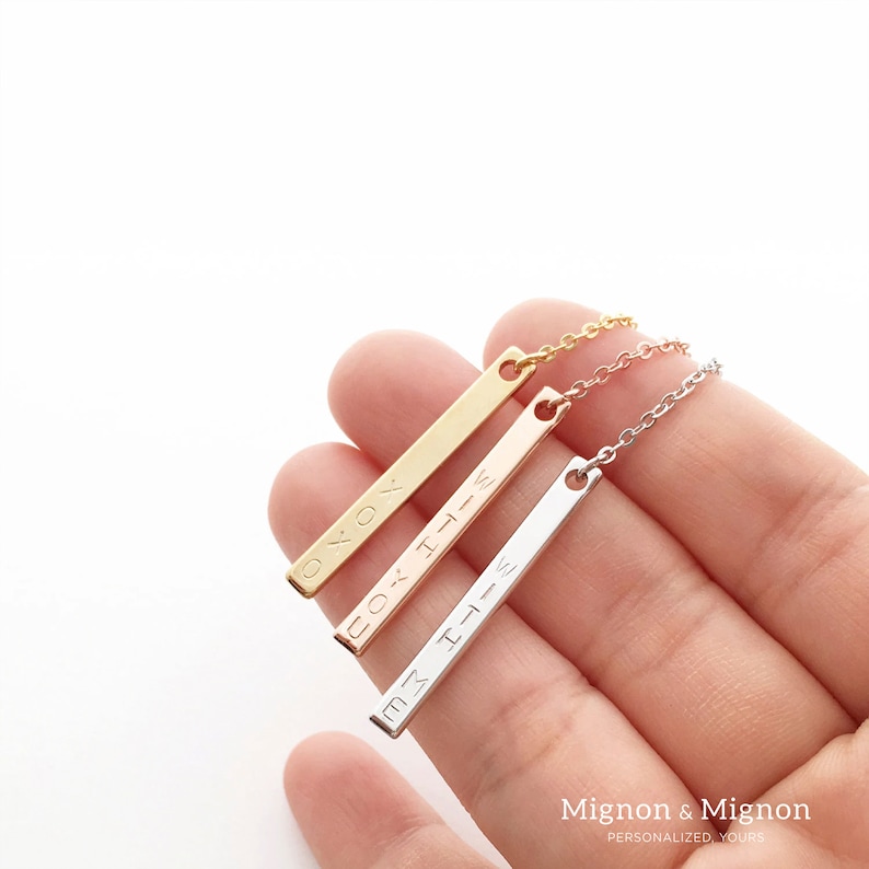 May include: Three gold bar necklaces with different engravings. The necklaces are in gold, rose gold, and silver. The engravings read "XOX", "Little", and "With You".