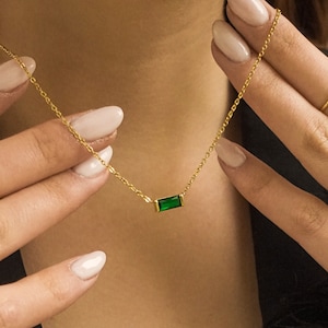 May include: A gold chain necklace with a small, rectangular green gemstone pendant.