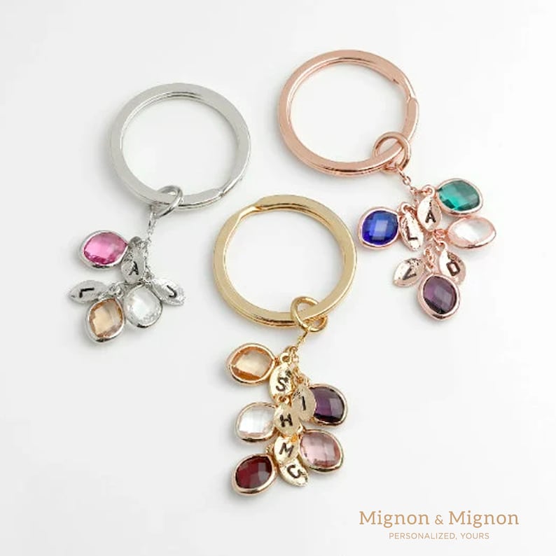 May include: Three keychains with different colored metal rings and charms. Each charm has multiple small stones with letters engraved on them. The stones are in various colors, including pink, blue, green, purple, and clear.