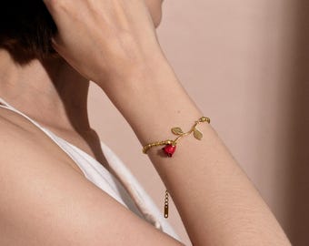May include: A gold bracelet with a red rose charm and delicate leaves. The bracelet is made of small gold beads and has an adjustable clasp.