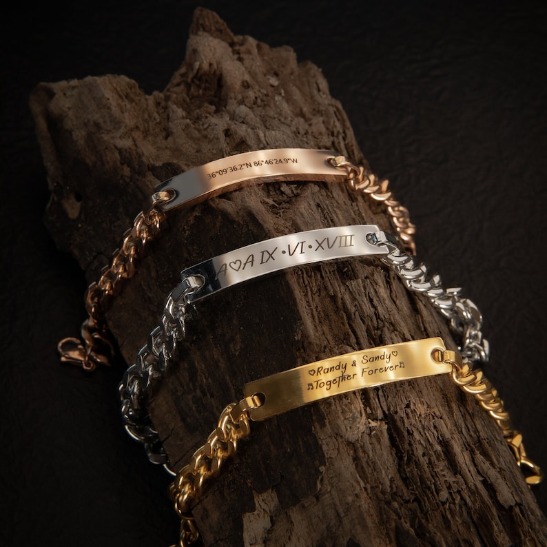 Pode incluir: Tr&ecirc;s pulseiras de ouro, prata e ouro rosa com mensagens gravadas. A pulseira de ouro diz "Randy & Sandy Together Forever". A pulseira de prata diz "SCAA IX &bull; VI-XVIII". A pulseira de ouro rosa diz "36&deg;09&prime;36.2"N 86&deg;46&prime;24.9"W".