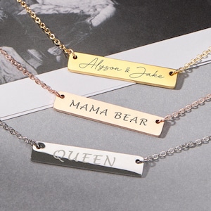 May include: Three personalized bar necklaces in gold, rose gold, and silver. The gold necklace reads "Alyson & Jake", the rose gold necklace says "MAMA BEAR", and the silver necklace says "QUEEN". Each necklace has a delicate chain.
