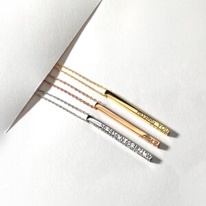 May include: Three silver bar necklaces with different engravings. The top necklace has the words "MISSING YOU" engraved on the bar. The middle necklace has the word "Alex" engraved on the bar. The bottom necklace has the coordinates "56.3456&deg;N 65.3821&deg;W" engraved on the bar.