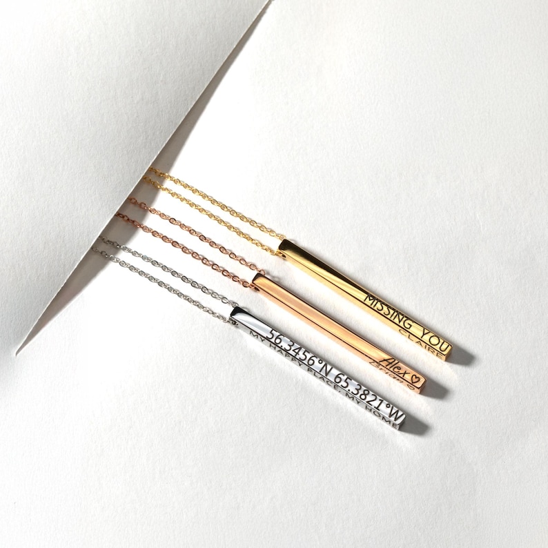 May include: Three silver bar necklaces with different engravings. The top necklace has the words "MISSING YOU" engraved on the bar. The middle necklace has the word "Alex" engraved on the bar. The bottom necklace has the coordinates "56.3456&deg;N 65.3821&deg;W" engraved on the bar.
