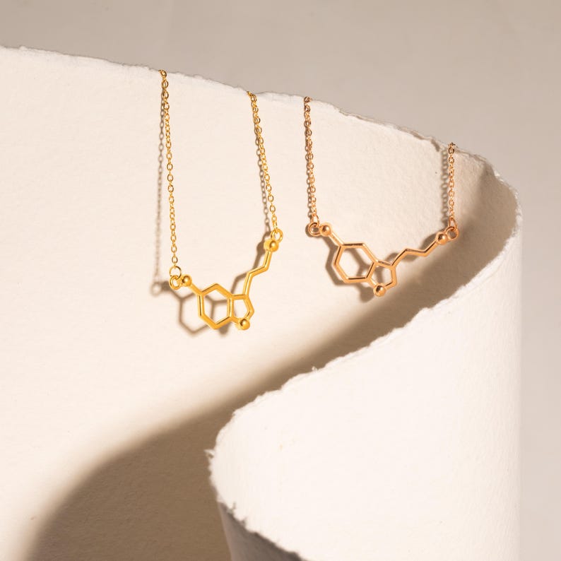 May include: Two gold necklaces with a chemical structure pendant. The pendant is a stylized representation of the molecule dopamine.