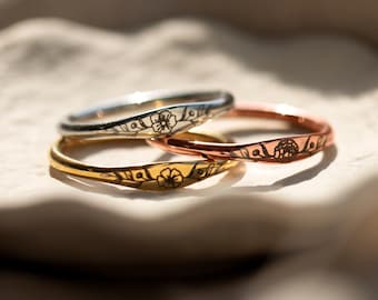 Op de afbeelding: Drie dunne ringen van goud, zilver en roségoud met een gegraveerd bloemenontwerp op elk.