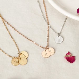 May include: Three gold necklaces with initial charms. The first necklace has three charms with the letters "S", "H", and "E". The second necklace has two charms with the letters "K" and "S". The third necklace has one charm with the letter "B".