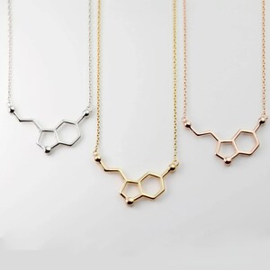 May include: Three necklaces with a silver, gold, and rose gold chain. Each necklace features a pendant in the shape of the chemical structure of dopamine.