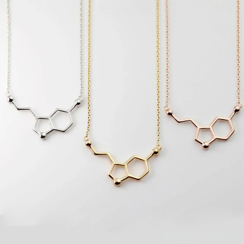 May include: Three necklaces with a silver, gold, and rose gold chain. Each necklace features a pendant in the shape of the chemical structure of dopamine.