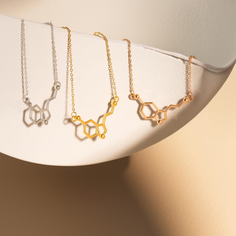 May include: Three necklaces with a chemical structure pendant. The necklaces are silver, gold, and rose gold. The pendant is a representation of the chemical structure of dopamine.