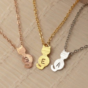 May include: Three gold necklaces with cat-shaped pendants. The pendants have the letters 'S', 'E', and 'A' engraved on them.