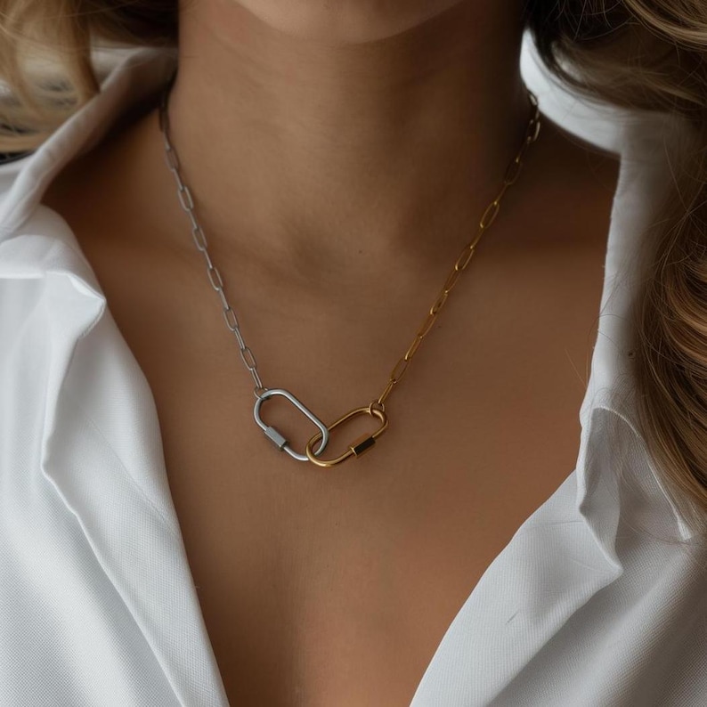 May include: A silver and gold chain necklace with two linked carabiner clasps. The necklace is worn by a person with a white shirt.