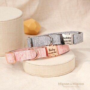 May include: Two personalized dog collars, one pink and one gray, with silver and rose gold buckles. The collars have the names "Bailey" and "Bobby" and phone numbers on the tags. The collars are on a beige fabric surface. Mignon & Mignon Personalized, Yours.