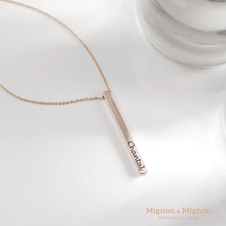 May include: A gold bar necklace with the name "Chantal" engraved on it. The necklace is on a white marble surface.