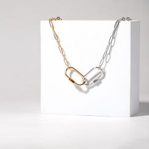 May include: A gold and silver chain necklace with two linked oval-shaped clasps. The necklace is displayed on a white surface.