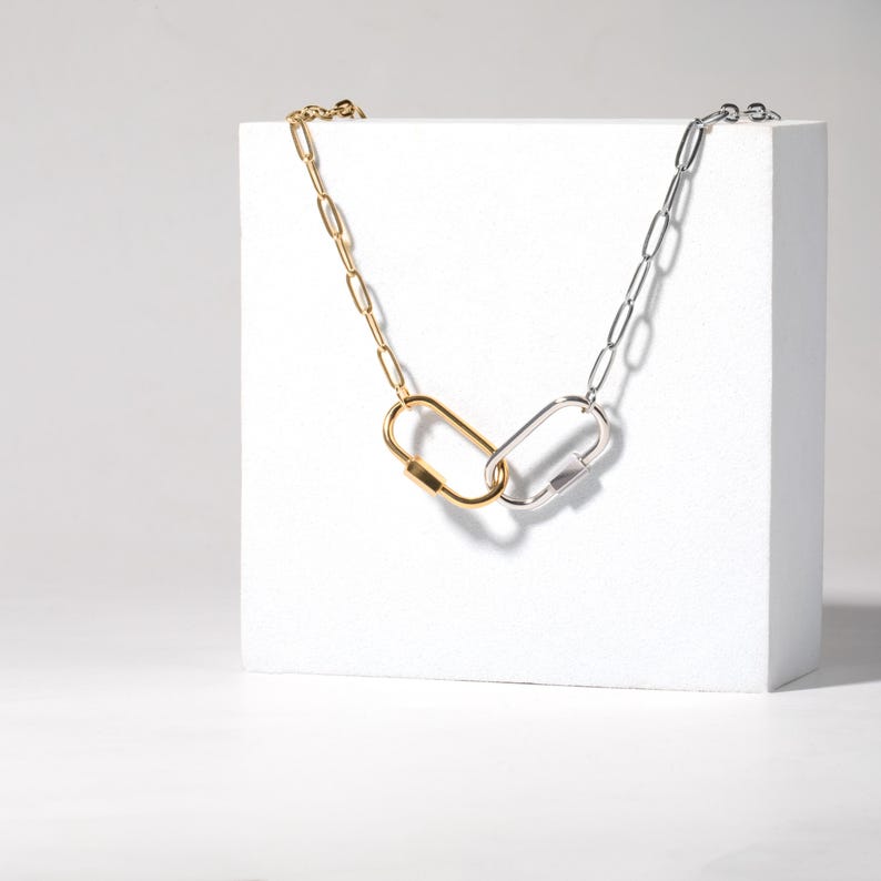 May include: A gold and silver chain necklace with two linked oval-shaped clasps. The necklace is displayed on a white surface.