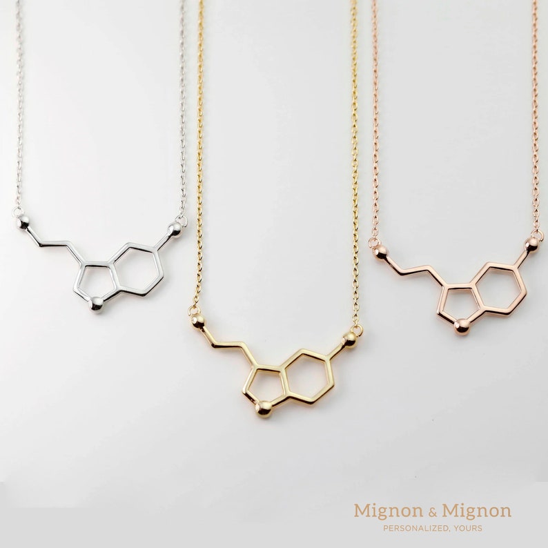 May include: Three delicate necklaces with a silver, gold, and rose gold finish. Each necklace features a pendant shaped like the chemical structure of the neurotransmitter dopamine.