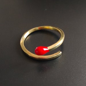 Puede incluir: Un anillo de oro con una cabeza de cerilla roja. El anillo está hecho de metal y tiene un diseño simple.