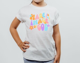 May include: White t-shirt with a colorful graphic that says "Made in the image of God" with flowers around the text.